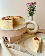 Layered biscoff pancake cake with a slice on a plate, next to a vase with flowers.