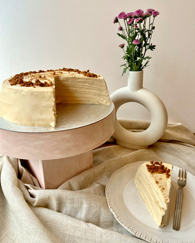 Layered biscoff pancake cake with a slice on a plate, next to a vase with flowers.