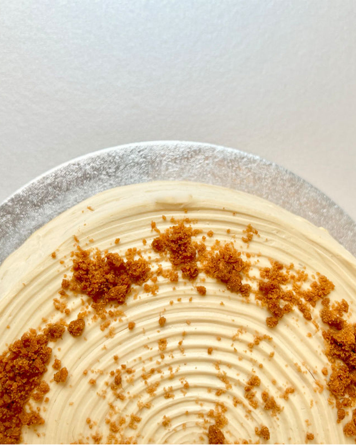 Close-up of a biscoff pancake cake with creamy topping and brown crumbly biscoff on a white background.