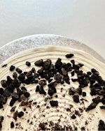 Close-up of a pancake cake with cream and cookie crumb toppings on a white background.
