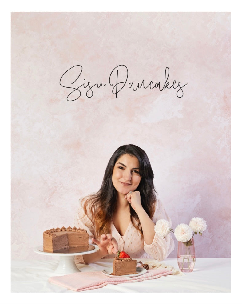 Book cover that has a woman sitting at a table with a cake and flowers, featuring 'Sisu Pancakes' text.