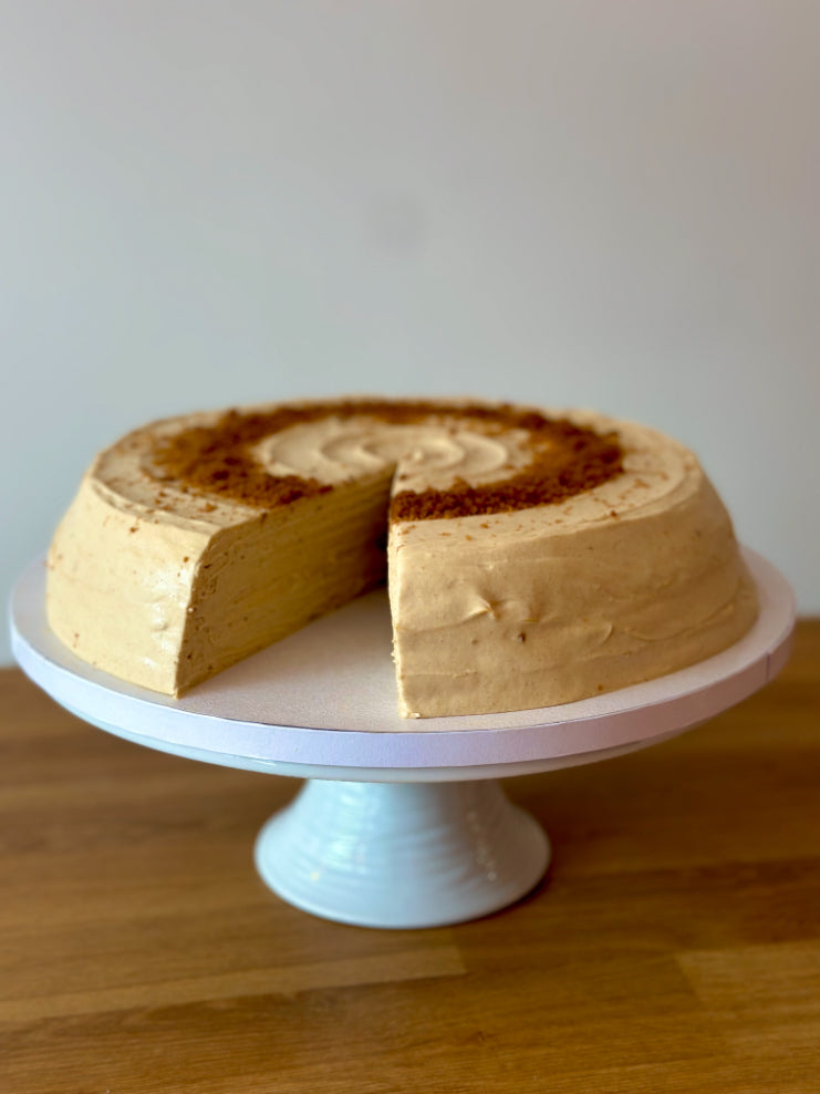 Round biscoff pancake cake with a slice taken out, sat on a white cake stand.