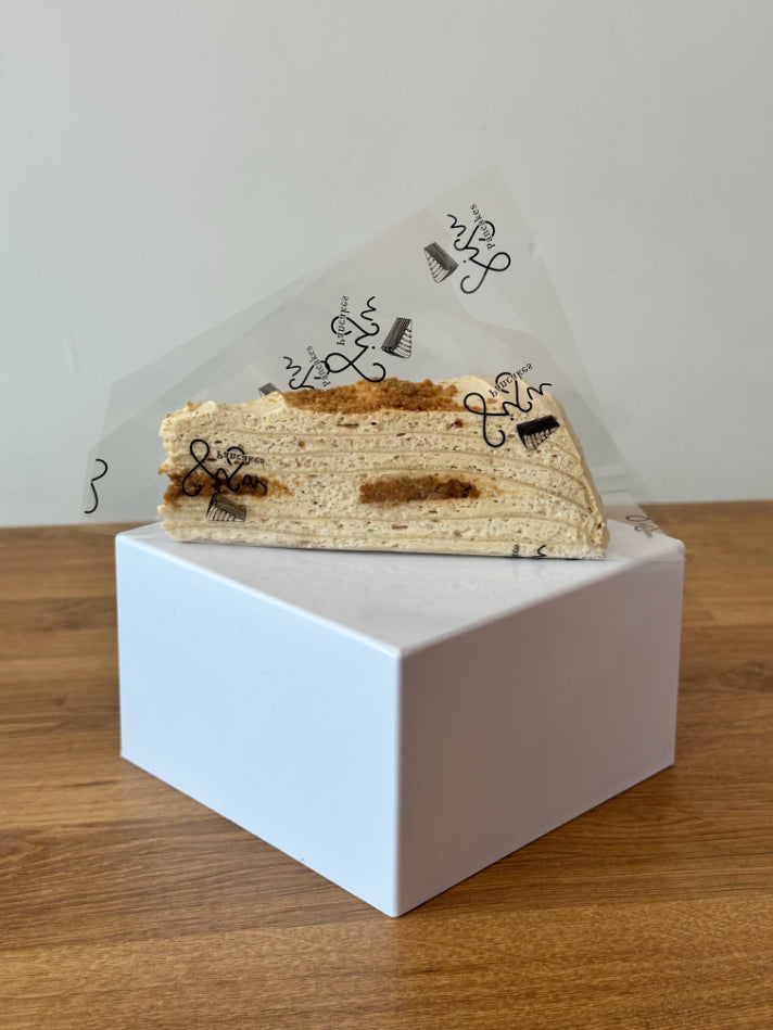 Slice of biscoff pancake cake in plastic packaging set on a white stand.