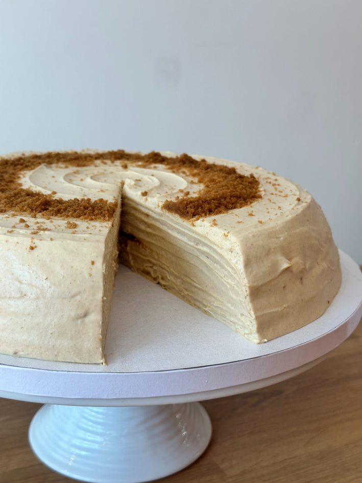 Close up of a biscoff pancake cake with a slice taken out, set on a white cake stand.