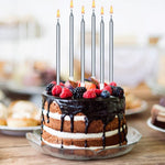 Chocolate cake with berries and six lit silver candles on a wooden table.