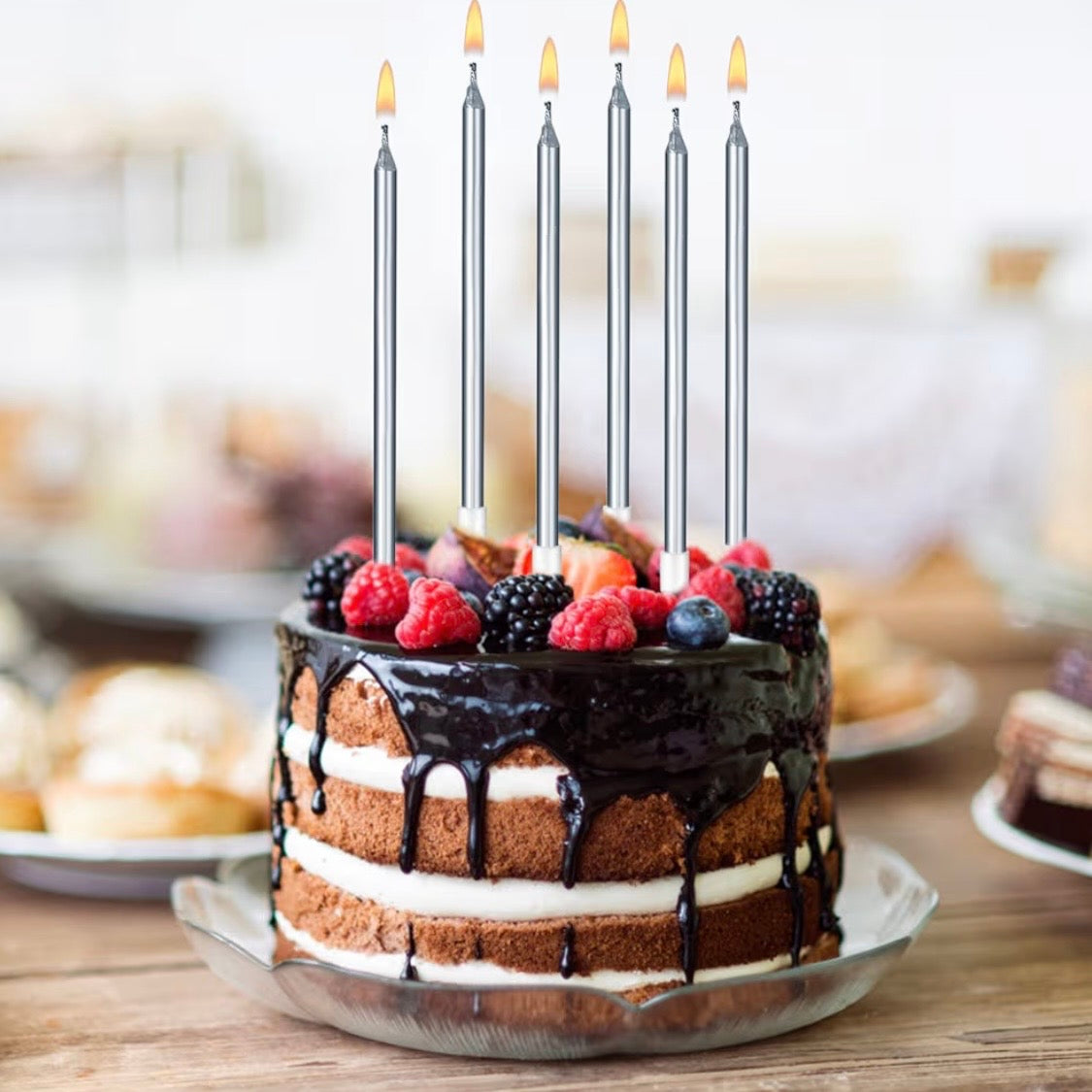 Chocolate cake with berries and six lit silver candles on a wooden table.