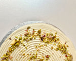 Close up of a pistachio pancake cake with pistachio nuts sprinkled on top of white frosting, set against a white background.
