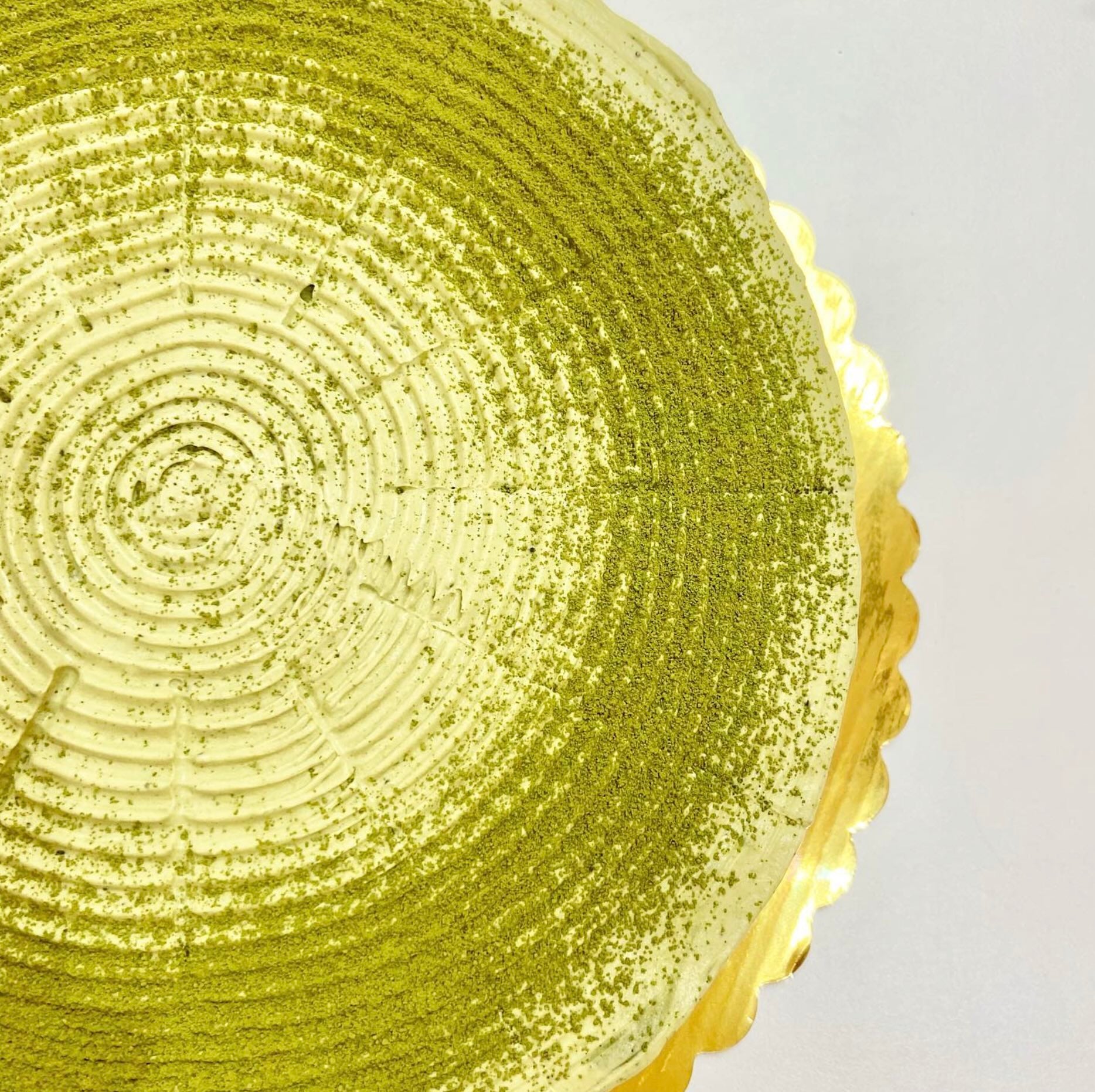 A close-up of a round matcha pancake cake with matcha powder sprinkled on top, sitting on a gold tray.