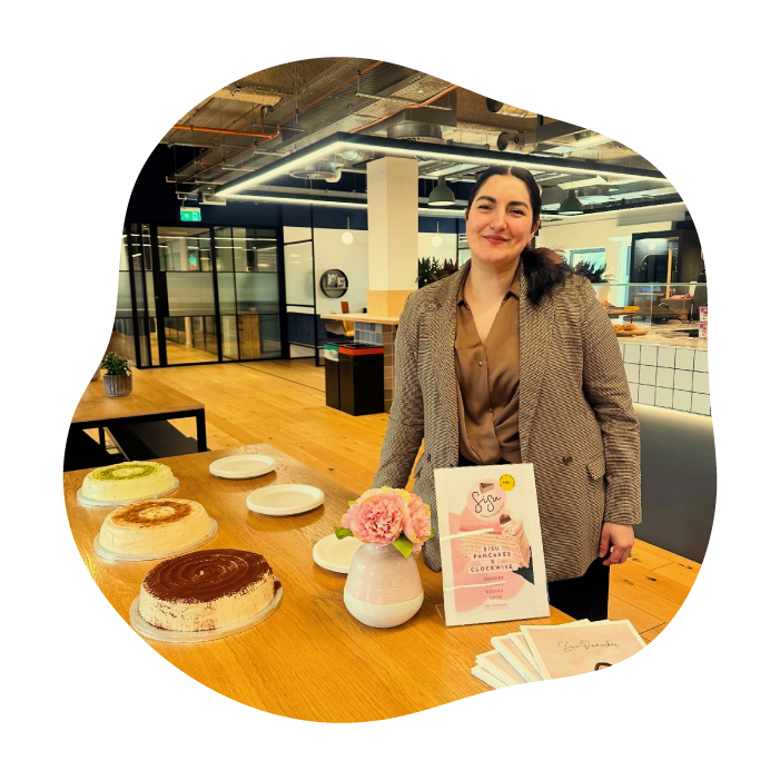 A woman stands behind a wooden table displaying several pancake cakes and a printed card in a modern office setting.