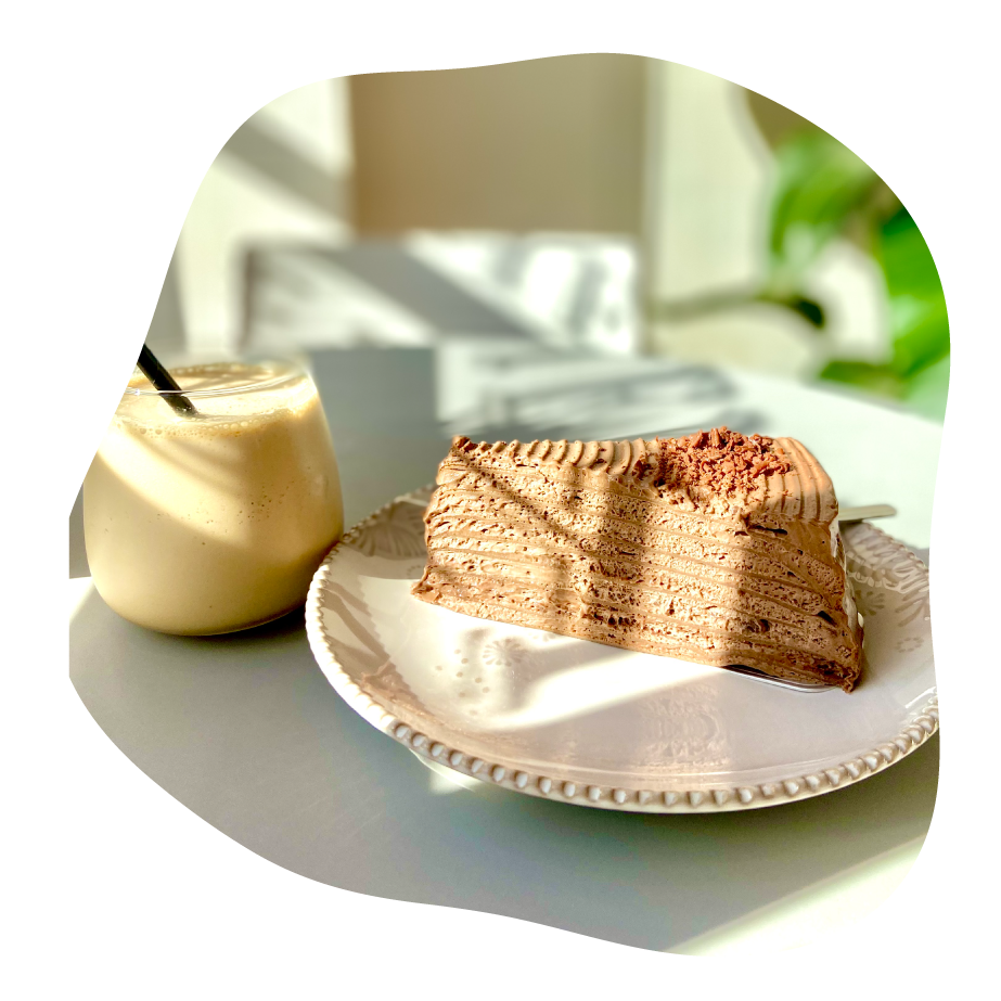 Slice of layered pancake cake with a smoothie, set against a blurred outdoor background.