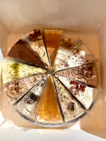 A round multi-slice pancake cake photographed from above inside a white box. The slices show different flavors and toppings.