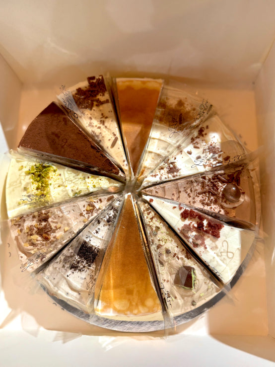 A round multi-slice pancake cake photographed from above inside a white box. The slices show different flavors and toppings.