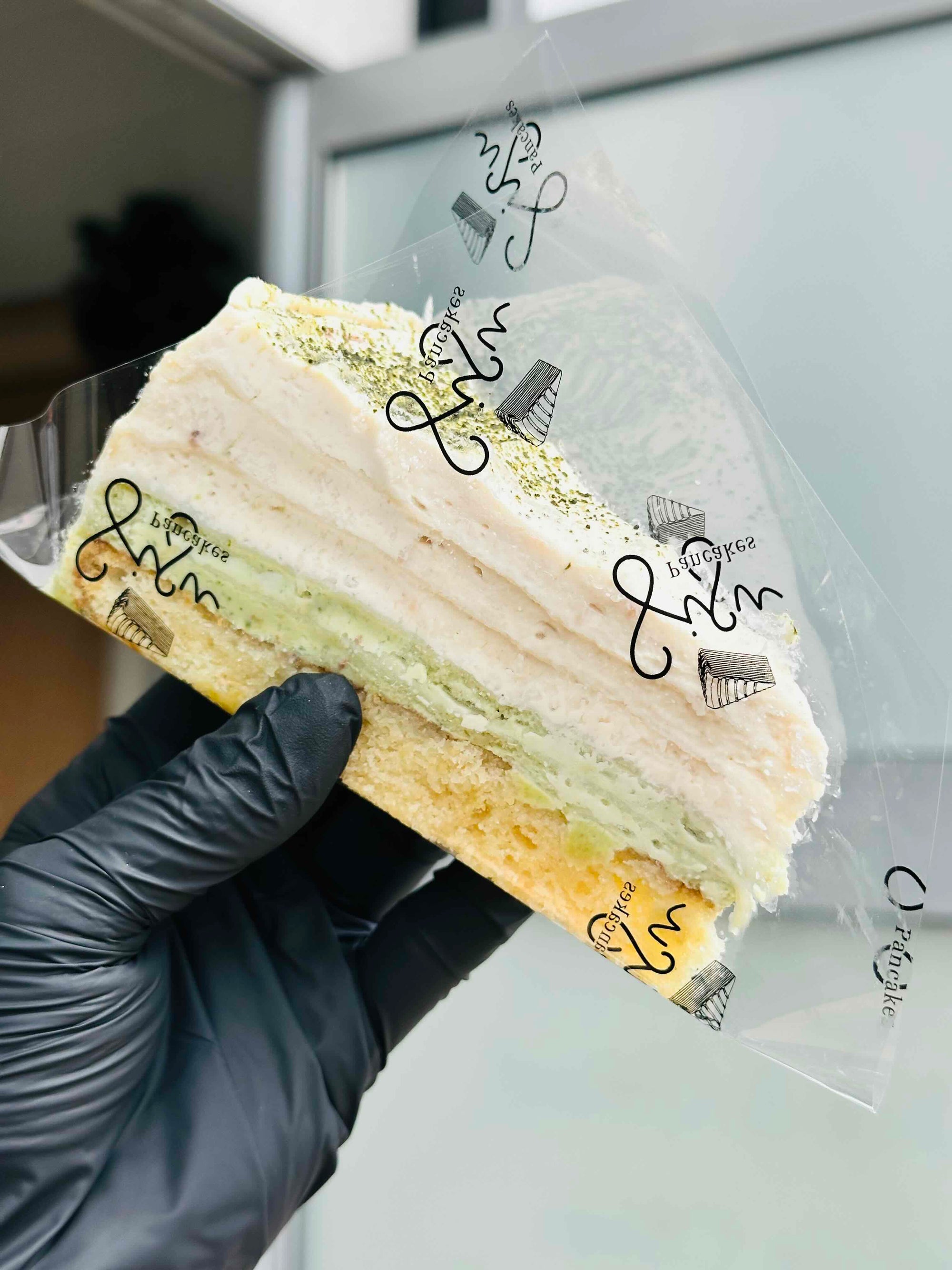 A hand wearing a black glove holds a pancake cake - matcha Strawberry