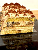 A layered pancake cake slice with cream-colored frosting, shown on a glossy black surface with a reflection.