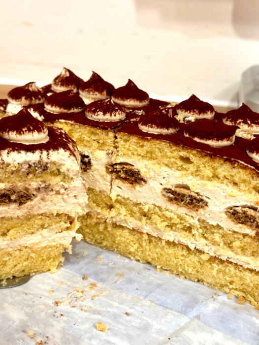 A close-up of a layered cake with golden sponge layers and cream-colored frosting, with a slice cut out.