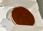 A round tiramisu pancake cake, presented inside an open white cardboard box.